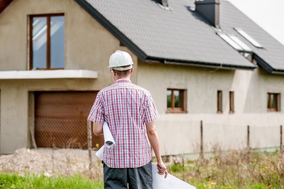 Un artisan casqué devant une maison en construction