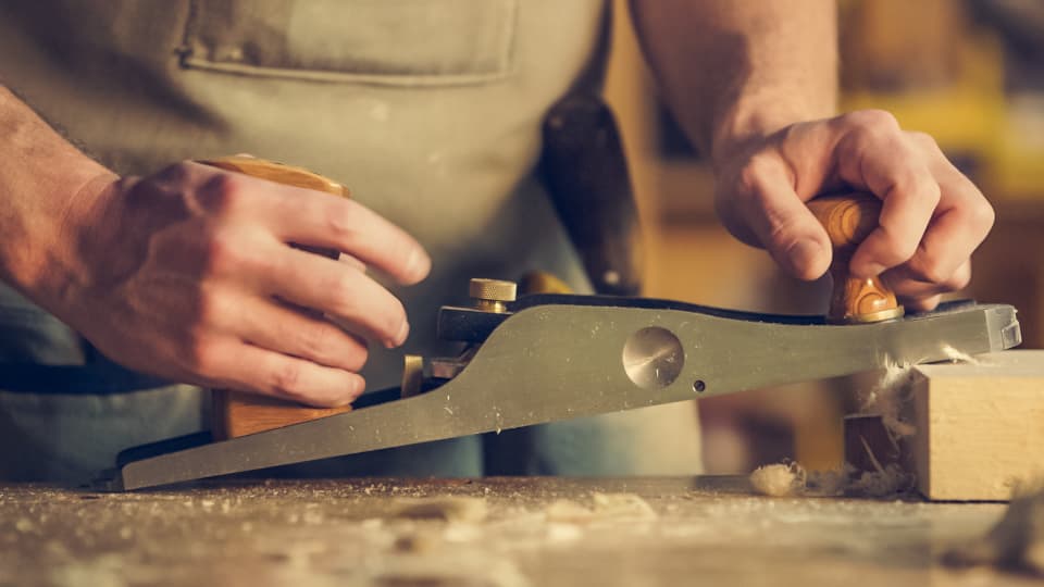 Un menuisier rabote une pièce de bois dans son atelier