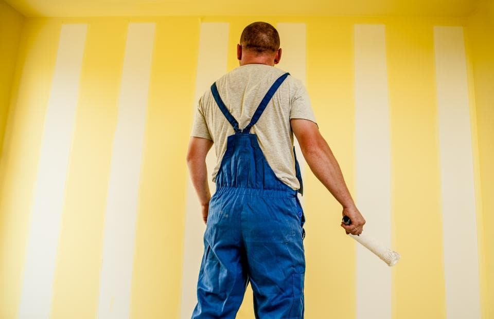 Un peintre en bâtiment devant un mur en cours de rénovation